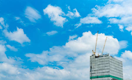 Construction site with crane and building. Real estate industry. Crane use reel lift up equipment in construction site. Building made of steel and concrete. Crane work against blue sky and white cloudの写真素材