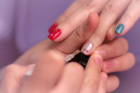 Woman receiving fingernail manicure service by professional  manicurist at nail salon. Beautician painting nails at nail and spa salon. Focused on white and glitter nail polish at nail salon.の写真素材
