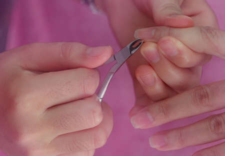 Woman receiving fingernail manicure service by professional  manicurist at nail salon. Beautician use clipper cleaning and cutting cuticle at nail and spa salon. Hand and nail therapy by therapist.の写真素材