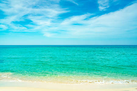 Golden sand beach by the sea with emerald green sea water and blue sky and white clouds. Summer vacation on tropical paradise beach concept. Ripple of water splash on sandy beach. Summer vibes.の写真素材