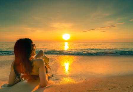Back view of sexy, enjoy and relax woman wear bikini lying on sand beach with straw hat relax and enjoy holiday at tropical paradise beach at sunset sky. Summer vacation. Holiday travel. Summer vibes.の写真素材
