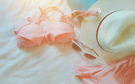 Top view of bikini swimsuit, sunglasses, and straw hat on bed sheet. Woman's swimwear and beach accessories on bed of resort. Pink bikini swimwear set for the beach. Summer vacation and summer vibes.の写真素材