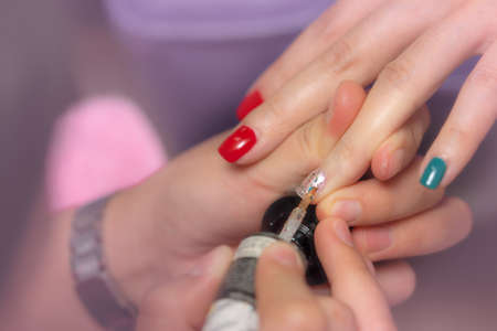 Woman receiving fingernail manicure service by professional  manicurist at nail salon. Beautician painting nails at nail and spa salon. Focused on white and glitter nail polish at nail salon.の写真素材