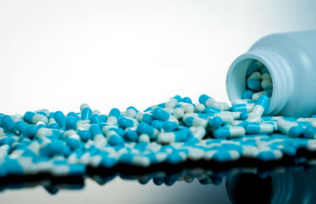 Blue and white capsule pill spilled out from white plastic bottle container. Global healthcare concept. Antibiotics drug resistance. Antimicrobial capsule pills. Pharmaceutical industry. Pharmacy.の写真素材