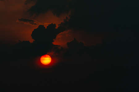 Red big sun in dark clouds. Devil sunset. Horror view of sun in black clouds sky. Summer sunset. Fiery sun in the evening. Nature background. Dramatic sky with big sun. Heat weather. Heaven concept.の写真素材