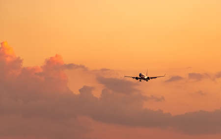 Commercial airline. Passenger plane landing at airport with beautiful sunset  sky and clouds. Arrival flight. Airplane flying in a line for landing. Aircraft open light in the evening flight.の写真素材