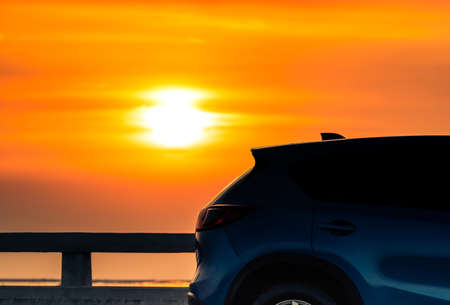 Blue compact SUV car with sport and modern design parked on concrete road by the sea at sunset in the evening. Hybrid and electric car technology concept. Car parking space. Automotive industry.の写真素材
