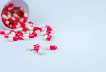 Pink and white capsules pill spilled out from white plastic bottle container. Global healthcare concept. Antibiotics drug resistance. Antimicrobial capsule pills. Pharmaceutical industry. Pharmacy.の写真素材