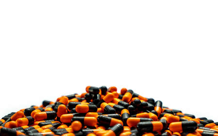 Closeup pile of orange-black capsule pills on white background. Vitamins and supplements. Pharmaceutical industry. Global healthcare concept. Capsule pills production. Drug over use in health system.の写真素材