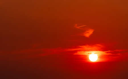 Beautiful red sun at sunset. Red sunset sky. The sun is obscured by some clouds at sunset. Big sun in the evening. Blood sky. Heat and hot weather. Dramatic sun light. Background for majestic.の写真素材