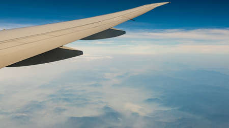 Wing of plane over mountain cover with fog and mist. Airplane flying on blue sky. Scenic view from...
