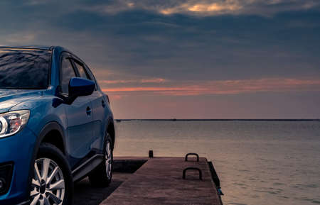Blue compact SUV car with sport and modern design parked on concrete road by the sea at sunset in the evening. Hybrid and electric car technology concept. Car parking space. Automotive industry.の写真素材