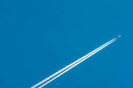 Airplane with white condensation tracks. Jet plane on clear blue sky with vapor trail. Travel by aeroplane concept. Trails of exhaust gas from airplane engine. Aircraft with white stripes.