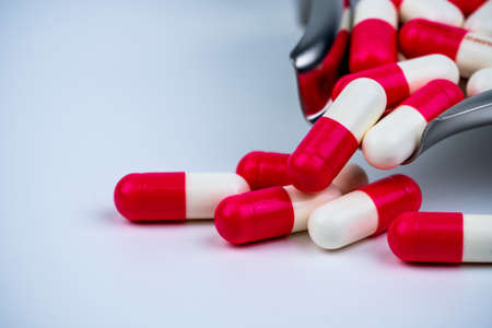 Red-white capsule pills on stainless steel drug tray and some on white table. Pharmacy drugstore background. Pharmaceutics concept. Pharmaceutical industry. Medicine in hospital. Global drug market.の写真素材