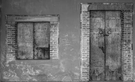 Old white and grey brick wall of ancient building. Concrete and brick building with closed wooden door and window. Exterior of old building. Cement and brick wall texture. Dirty house door and window.の写真素材