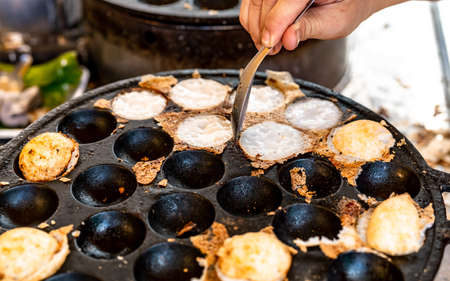 Mortar toasted pastry or Kanom Krok is Thai traditional dessert. Woman hand removing Kanom Krok from...