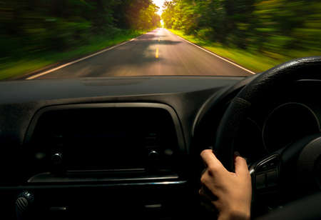 Driver hand holding steering wheel for control car. Inside view of car. Dashboard and windshield. Driving car on asphalt road with motion blur in the green forest. Perspective view fast car on highwayの写真素材