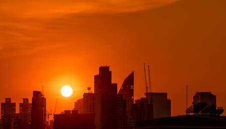 Business building in downtown at dusk with beautiful sunset sky. Silhouette of condo and apartment in the evening. Cityscape of skyscraper building and construction crane. Big sun with red sky.の写真素材