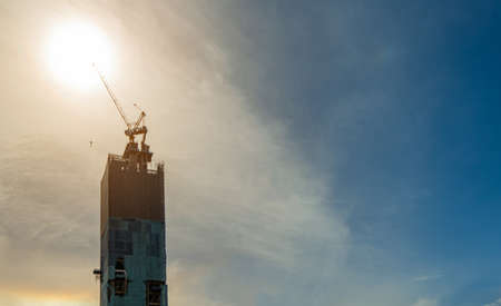 Construction site with crane and building. Real estate industry. Crane use reel lift up equipment in construction site. Building made of steel and concrete. Crane work against sky with sunlight.の写真素材