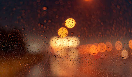 Orange night light bokeh from street light on traffic jam day. Rainy day. Transparent glass window...