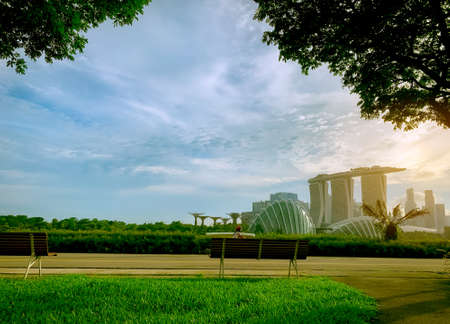 Landscape of hotel and business building. Empty wooden bench in Singapore public park. Cityscape of Singapore modern and financial city in Asia. Marina bay landmark of Singapore. Child riding bicycleのeditorial素材