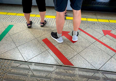 Passenger standing at railway platform waiting for board the high speed electric train at subway station. Modern train transport. Tourist standing at floor paint red arrow sign. Urban travel lifestyleの写真素材