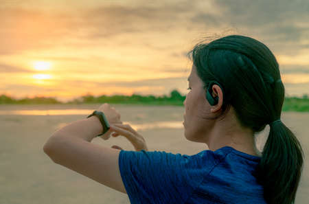 Asian woman wear in ear sport true wireless earbuds touching smart band after running in the...