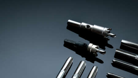 Closeup straight flute tap tip and hole saw on dark background.  Industrial tapping tools. Carbide...