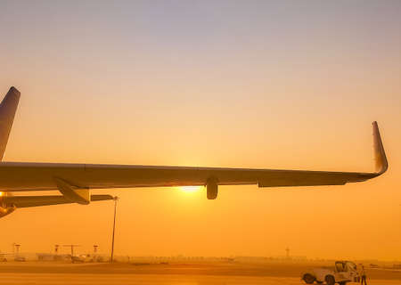 Closeup airplane wing with golden sunrise sky. Plane parked at airfield of airport. Morning flight....