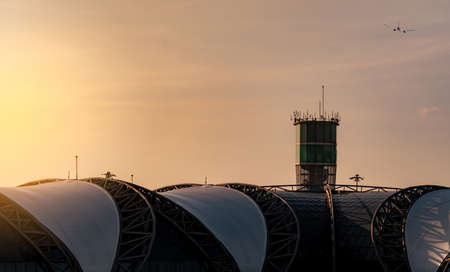Airport roof and air traffic control tower in the airport with international flight plane flying on the sky. Airport traffic control tower for control airspace by radar. Aviation technology.のeditorial素材