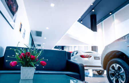 Fake red flowers in vase on table in modern car showroom. Car dealership interior building....