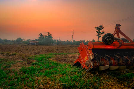 Ridging crackdown machine. Supply for tractor. Agricultural machinery in agriculture farm. Rice farm in morning with red sunrise sky. Nature of farmland. Farmer hut and electric pole in farmland.の写真素材