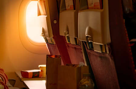 Food in brown paper bag put on plastic airplane tray table at seat back with blurred passenger hand...