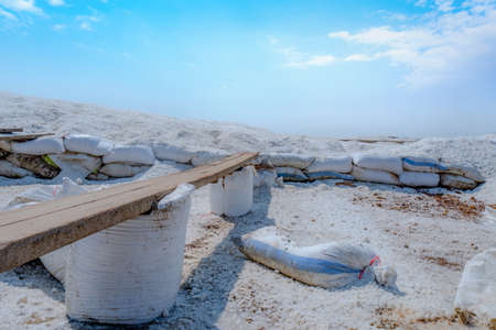 Brine salt farm with blue sky and white clouds. Pile of organic sea salt near warehouse. Raw material of salt industrial. Ocean salt. Summer travel in Thailand concept. Sodium chloride mineral.の写真素材