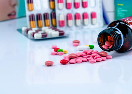 Tablets pills spread out of amber glass drug bottle on blurred capsules in blister pack. Red and pink tablets. Medication use concept. Painkiller medicine. Pharmaceutical industry. Pharmacy products.の写真素材