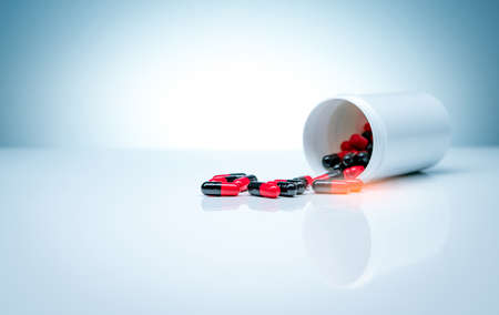 Red-black antibiotic capsule pills spread out of plastic drug bottle on white background. Pharmaceutical industry. Antibiotic drug resistance. Pharmaceutical manufacturing. Antimicrobial drug pills.の写真素材