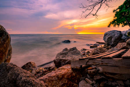Rock beach with blue and golden sunset sky. Skyline between sea water and sky in the evening. Calm ocean with soft wave. Summer travel at tropical sea and stone beach. Beauty in nature. Seascape.の写真素材