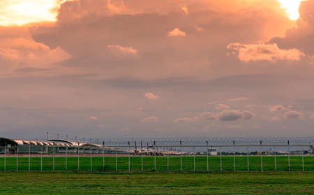 Landscape of green grass field and fence of the airport and beautiful sunset sky. Commercial airplane parked at apron of airport. Coronavirus impacted aviation business. Fence for safety and security.の写真素材