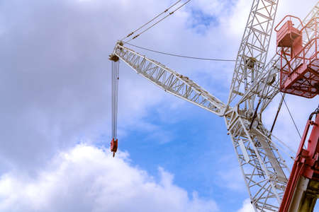 Crawler crane against blue sky and white clouds. Real estate industry. Red-white crane use reel lift up equipment in construction site. Crane for rent. Crane dealership for construction business.のeditorial素材