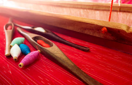 Selective focus on green, pink, blue, white yarn in weaving shuttle tool on weaving machine. Textile fabric weave. Weaving using traditional weaving loom and shuttle. Textile or cloth production.の写真素材