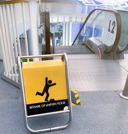 Beware uneven floor warning sign on yellow board in front of escalator in shopping mall. Beware uneven floor warning sign for safety at walkway before dawn way of escalator. Notice for safety.の写真素材