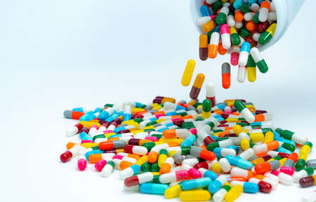 Pouring capsule pills from plastic drug bottle to white table. Pile of colorful capsule pills....
