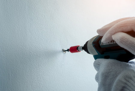 People hand drilling screw into apartment wall with cordless drill. People wear white gloves and hand holding drilling tool for apartment renovation. Person working home improvement with DIY concept.の写真素材