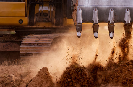Selective focus on metal bucket teeth of backhoe digging soil. Backhoe working by digging soil at...