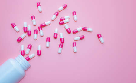 Pink-white capsules pill spilled out from plastic bottle container on pink background. Antibiotics drug resistance. Antimicrobial capsule pills. Pharmaceutical industry. Pill for happy love concept.の写真素材