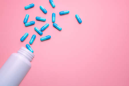 Blue capsule pills spread out of white plastic drug bottle on pink background. Pharmacy banner....