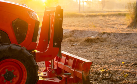 Orange tractor parked at rice farm in summer morning with sunlight. Agricultural machinery in agriculture farm. Smart farming concept. Vehicle in farm. Labor saving machinery. Equipment for plantationの写真素材