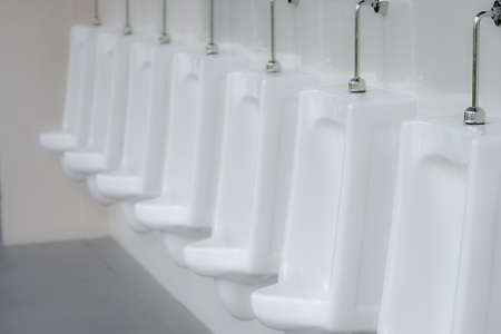 White urinals in men public toilet. Ceramic urinals in a row in men restroom. Man bladder health...
