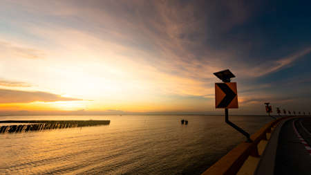 View from curve road to sunset skyline over the tropical sea in Thailand. Calm sea with yellow sunset sky. Beauty in nature. Road beside the sea in summer. Summer road trip travel concept. Tranquilityの写真素材