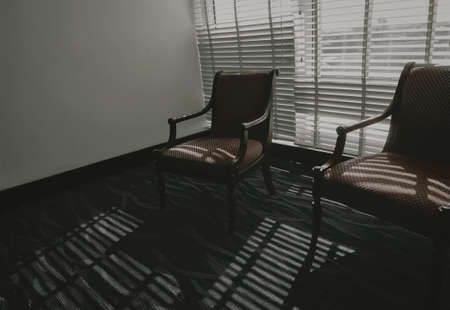 Empty chairs with light and shadow in the room. Furniture for home decoration in vintage style. Empty couple of chair in living room stand on carpet floor near Venetian plastic blinds. Wooden chair.の写真素材